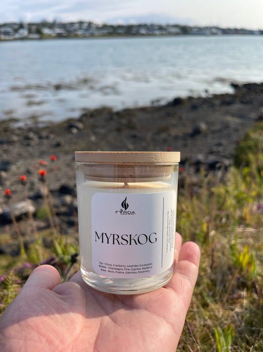 MYRSKOG candle with wooden lid resting on lush green moss in forest floor, top-down view, natural setting