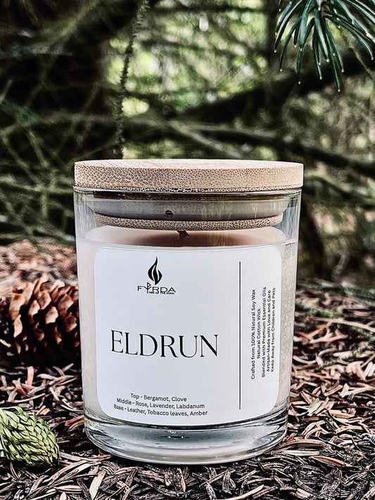 Eldrun soy candle with wooden lid on forest floor with pine needles and cones, peaceful woodland setting