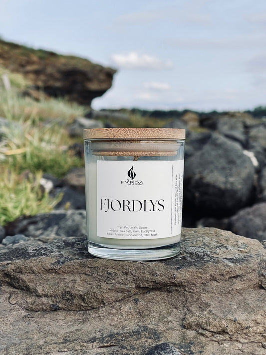FJORDLYS soy candle with wooden lid standing on coastal rock with cliff and blue sky in the background