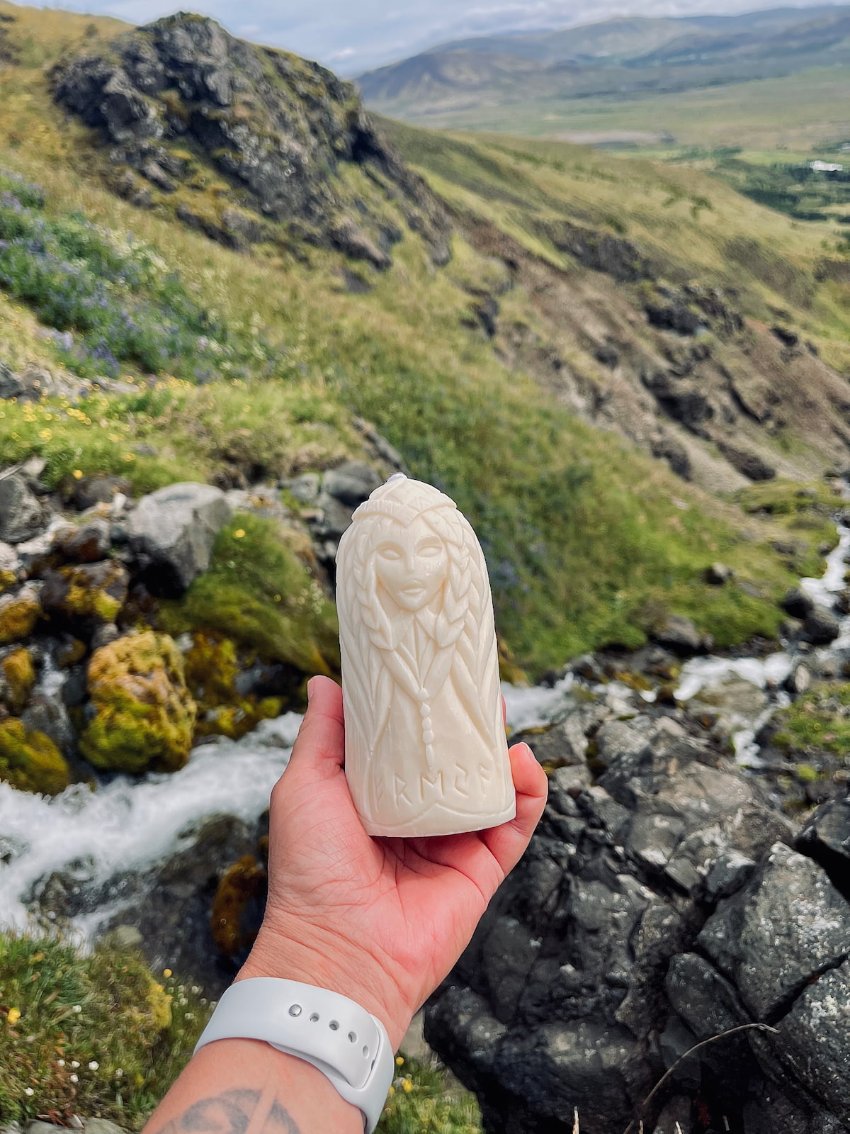 Hand holding Freya soy wax candle with Norse goddess design — mountain landscape view
