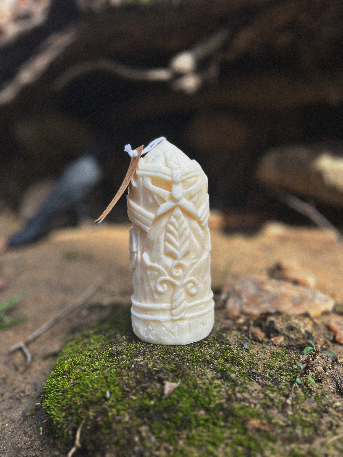 Odin candle with Viking mask design placed on mossy stone in forest, raven in background symbolizing Norse mythology